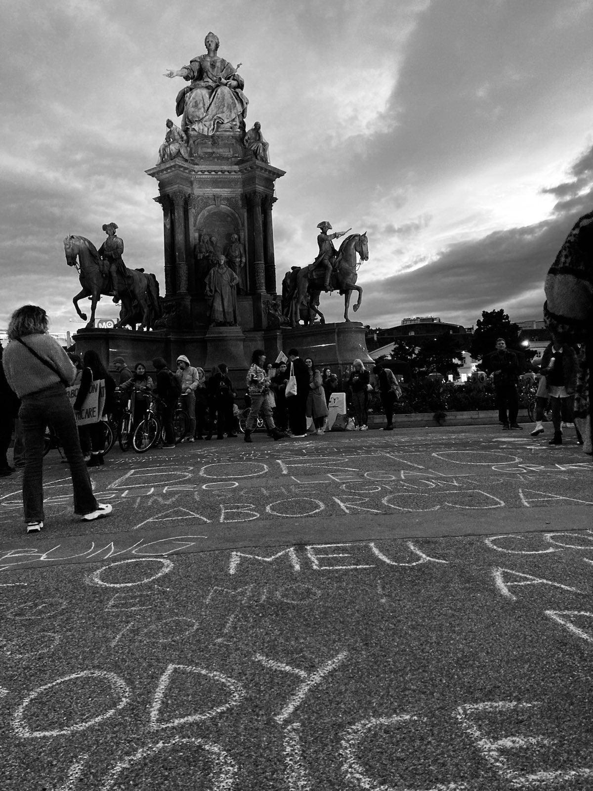 Schwarz-weiß-Bild der Maria-Theresien-Statue, davor Kreideaufschriften auf dem Asphalt